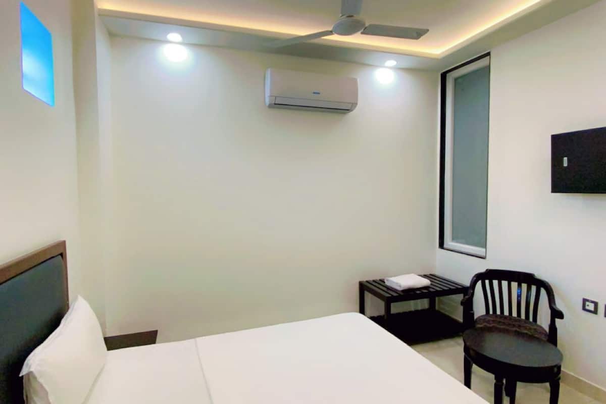 Una camera d'hotel con un letto, una sedia, un tavolino, un climatizzatore e una TV a parete.