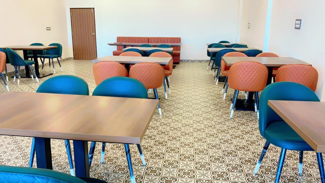 A classroom with tables and chairs, patterned carpet, and a wooden door.