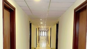 A long, narrow hallway with wooden doors on both sides and a shiny, reflective floor. - Hotel Giriraj Palace (Jaipur)