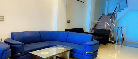 A modern living room with a blue sectional sofa, a glass coffee table, and a staircase with a metal railing.