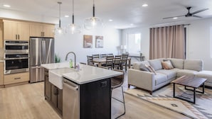 A modern kitchen with stainless steel appliances, a dining area with a table and chairs, and a living room with a sofa and a coffee table. - Stylish Poolside 3BR w/ Game Room & Pool Table (St. George)