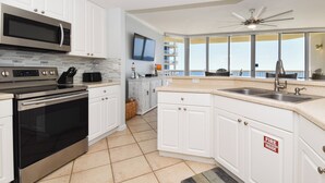 A modern kitchen with white cabinets, stainless steel appliances, a large window, and a ceiling fan. - Spacious Condo with Private Beach Access and Stunning Gulf and Resort Views (Destin)