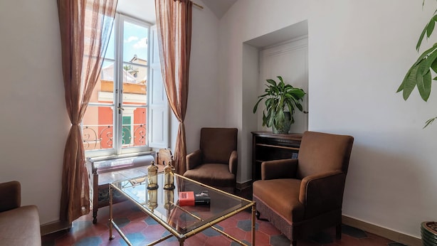Una sala de estar con una mesa de centro de vidrio, dos sillones marrones, una planta en maceta y vistas a un balcón con barandillas anaranjadas.