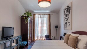Una habitación de hotel con una cama grande, un televisor sobre un soporte, una silla, un escritorio y una planta.