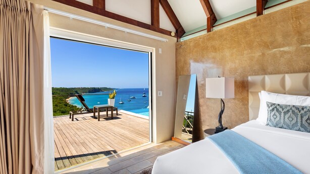 Ein Schlafzimmer mit großem Fenster mit Blick auf einen Strand und das Meer.