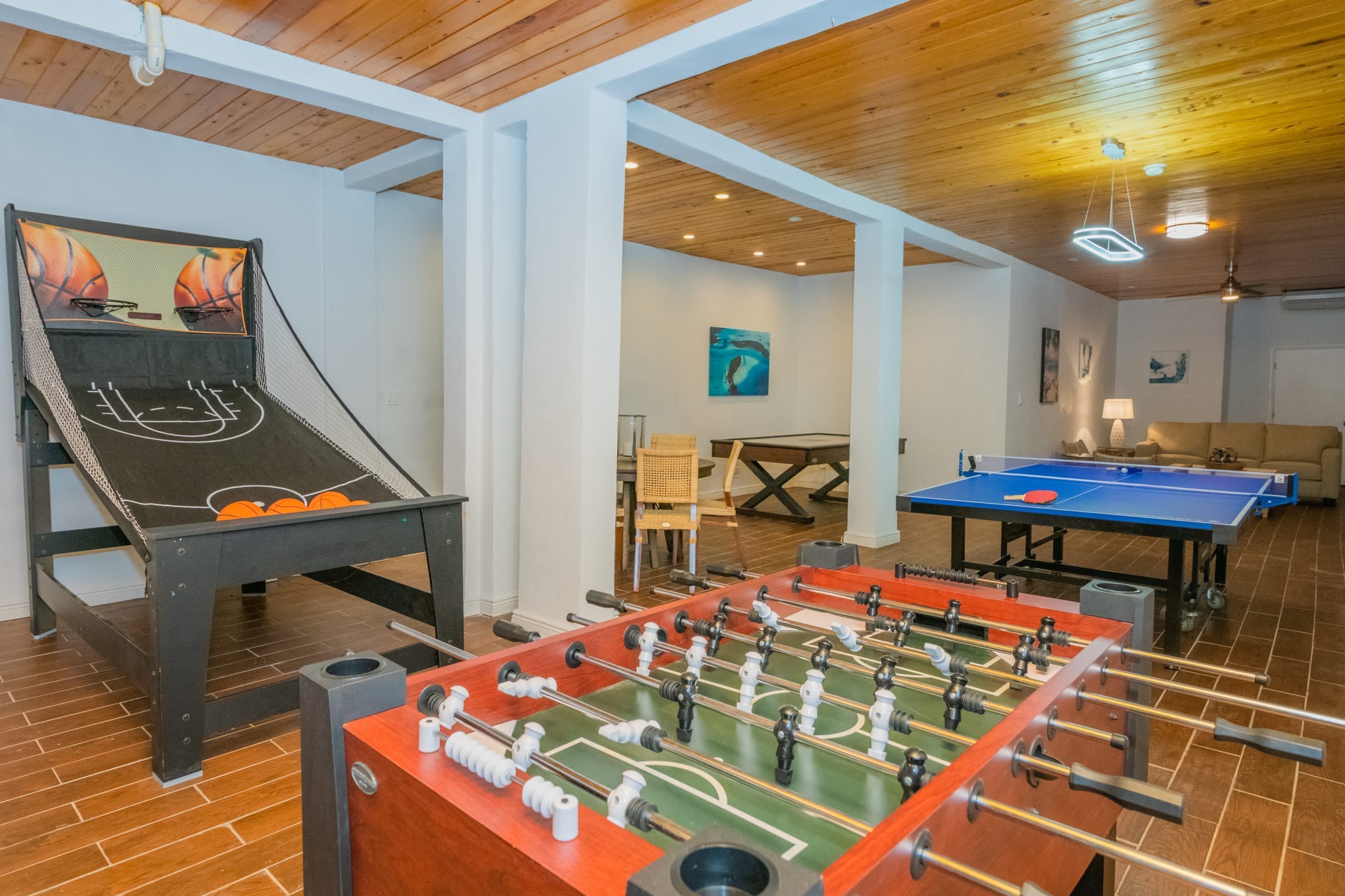 A room with a foosball table, a ping pong table, and a foosball table with a basketball court design.