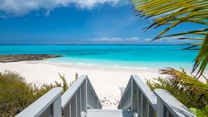 Egy strand, ahol egy fából készült sétaút vezet a partra, és amelyet zöld növényzet vesz körül.
