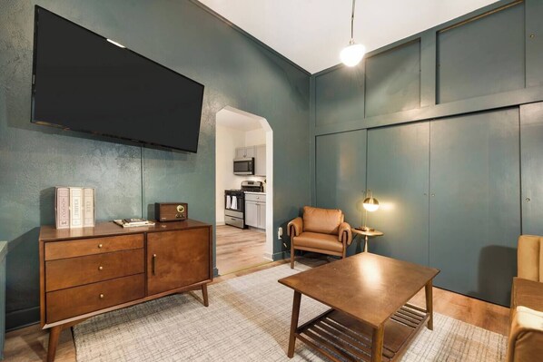 Een moderne woonkamer met een flatscreen televisie, een houten salontafel, een leren fauteuil en een bijzettafeltje met een lamp.