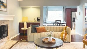 Un salon avec un canapé, une table basse, une cheminée et une cuisine en arrière-plan.