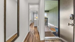 A hallway with wooden flooring, a door with a keypad lock, and a view into a room with a balcony. - Sea The Good 2 Bedroom Condo by RedAwning (Carolina Beach)