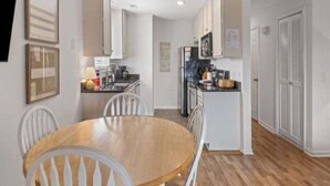 A compact kitchen with white cabinets, a wooden dining table, and a refrigerator. - Sea The Good 2 Bedroom Condo by RedAwning (Carolina Beach)