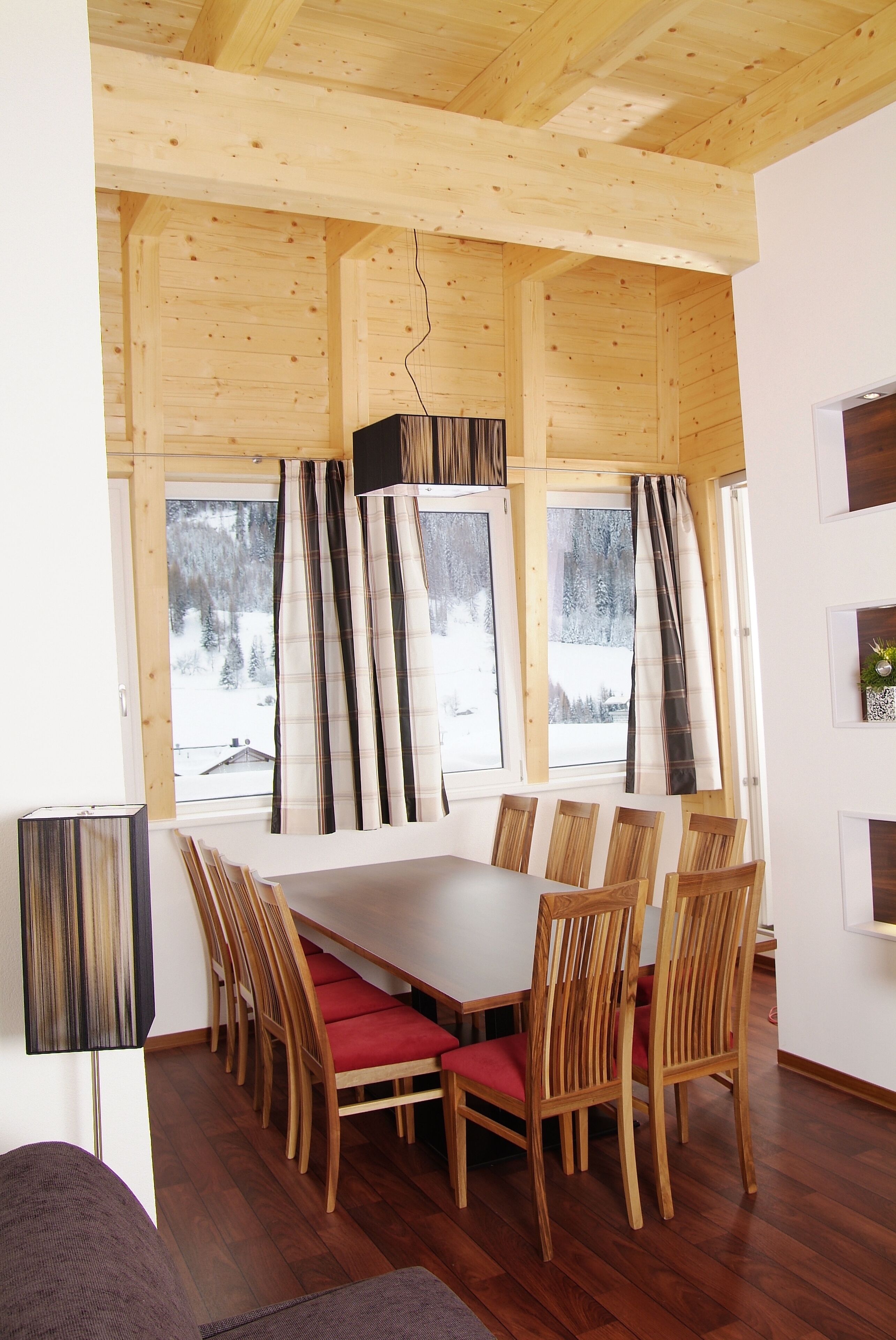 A wooden-paneled room with a large dining table and chairs, large windows with curtains, and a fireplace.
