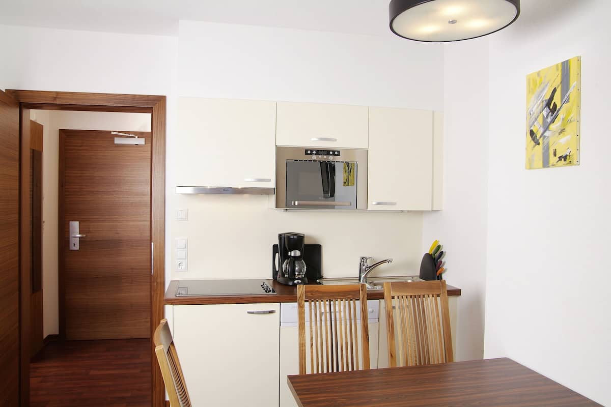 A compact kitchen with a microwave, coffee maker, and wooden chairs.