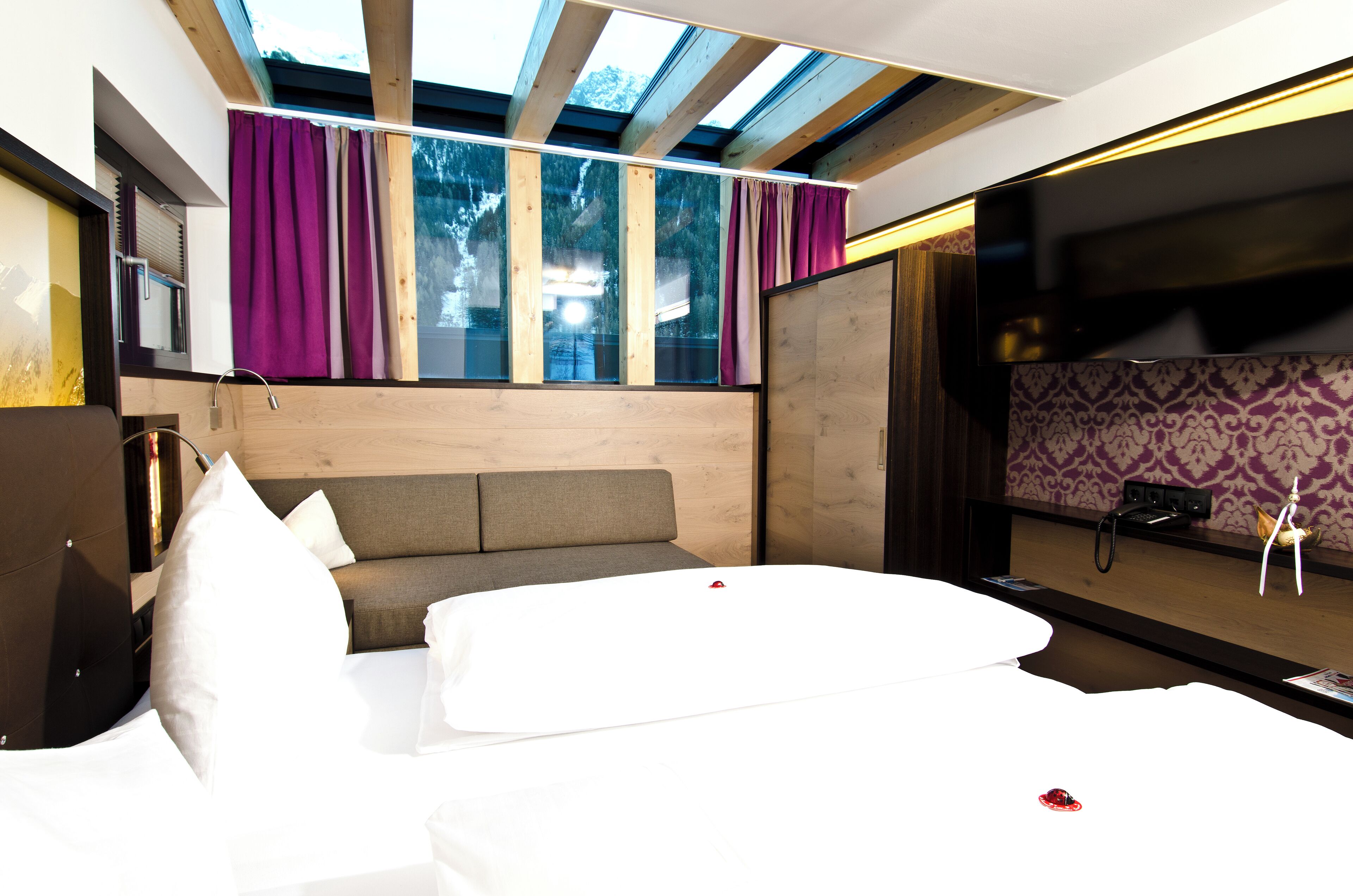 Habitación de hotel moderna con una cama grande, un sofá, un escritorio y vistas al exterior a través de amplias ventanas.