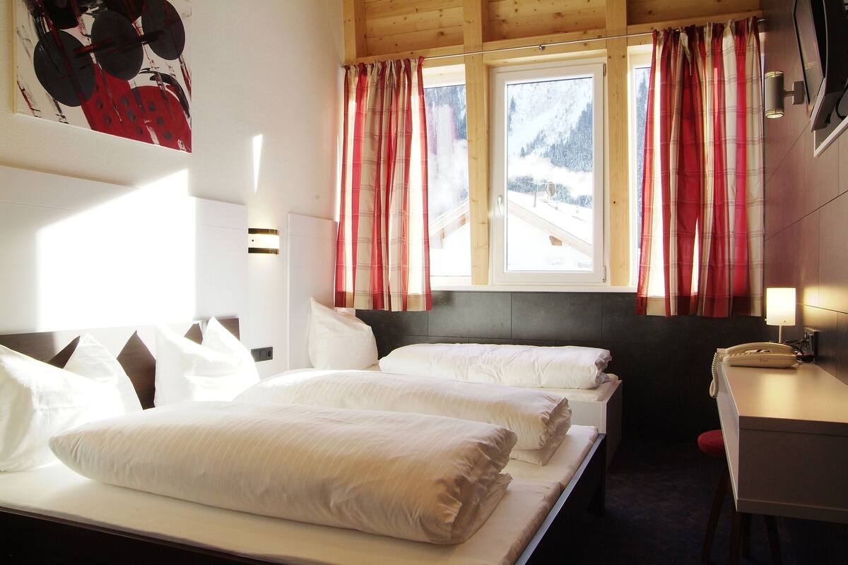 A hotel room with two beds, a desk, and a window with curtains.