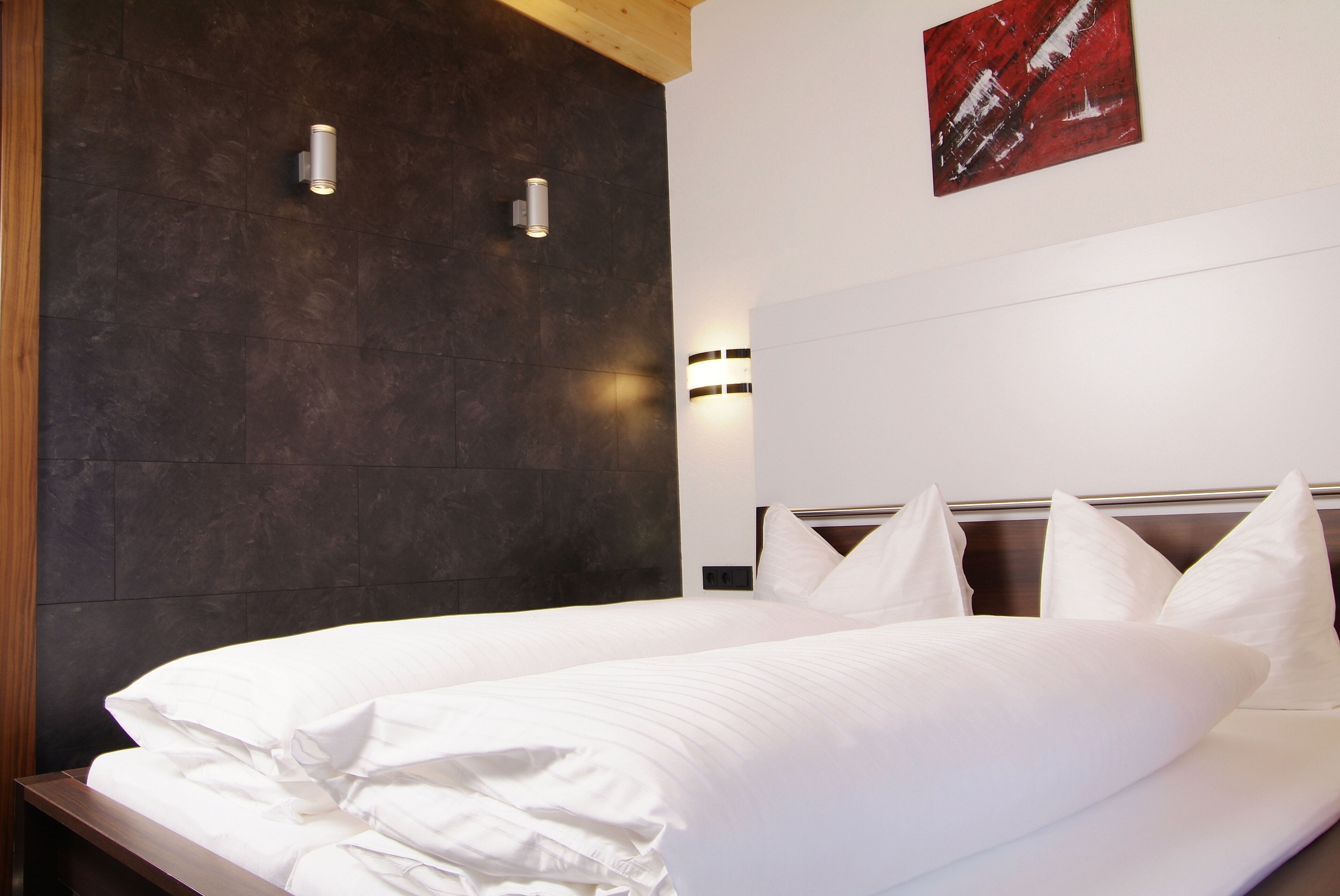 Een moderne hotelkamer met een groot bed, donkere wandbekleding en twee wandlampen.