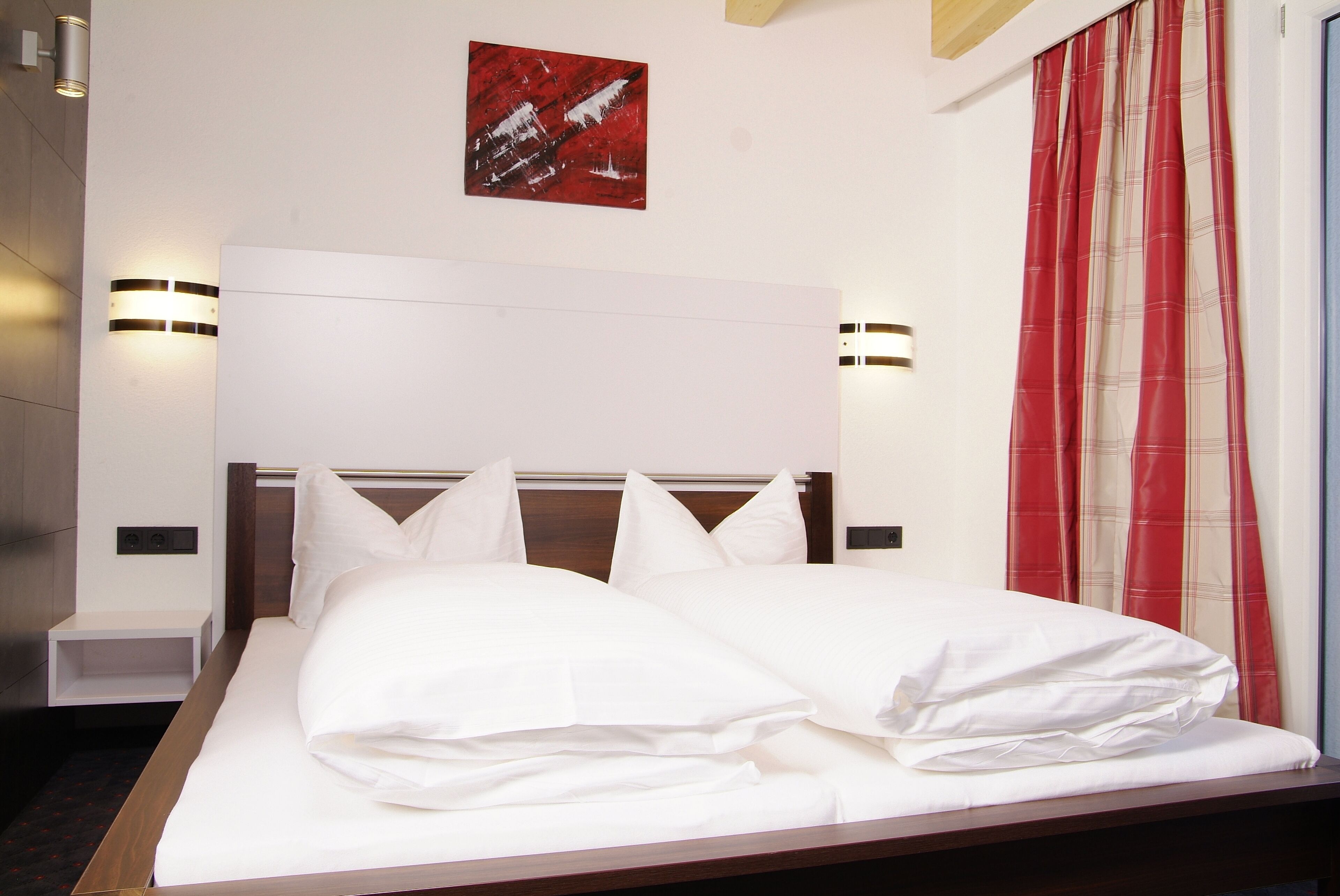 A neatly made bed with white linens, a wooden headboard, and two wall-mounted light fixtures.
