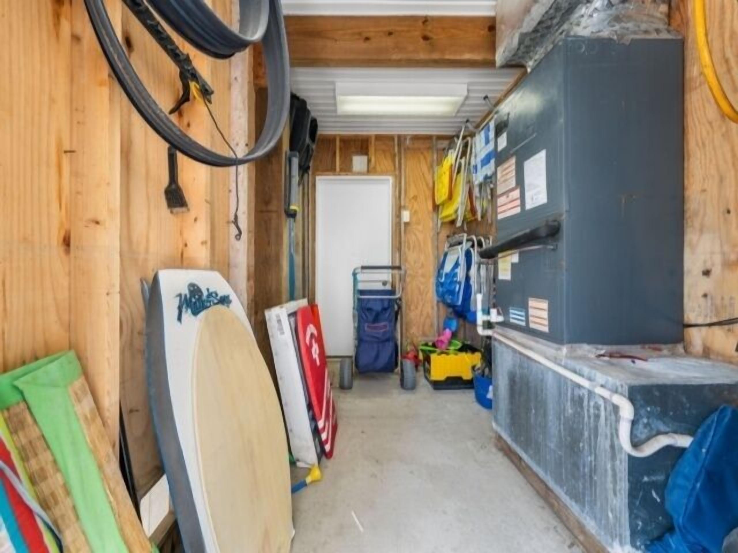 A narrow hallway with wooden walls, a whiteboard, and various items like surfboards and bags on shelves.