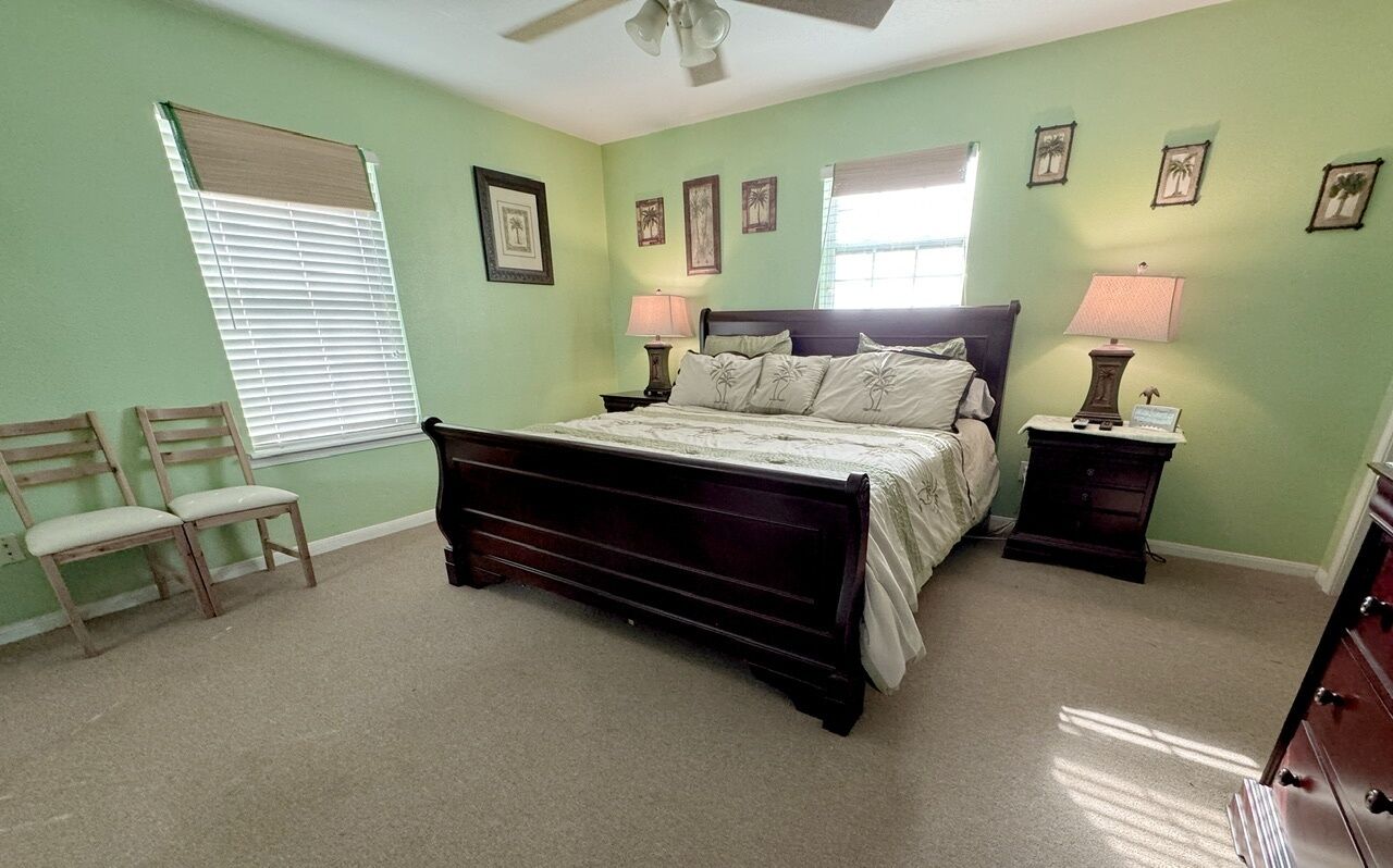 A bedroom with a bed, two nightstands, a chair, a dresser, and a window with blinds.