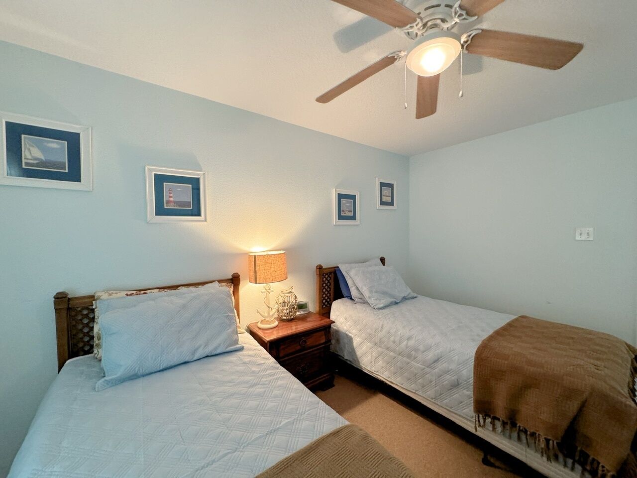 A bedroom with two beds, a ceiling fan, and framed pictures on the wall.
