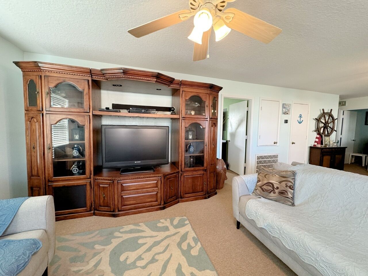 A living room with a wooden entertainment center, a flat-screen TV, a ceiling fan, and a white sofa.