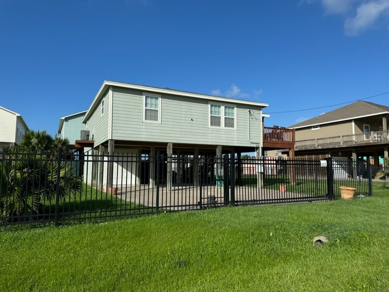 A two-story house with a covered patio area, surrounded by a black metal fence and a grassy yard.
