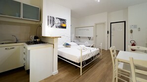 Una habitación de hotel compacta con kitchenette, una cama, un escritorio y una silla.