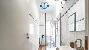 Un baño moderno con cabina de ducha de vidrio, un espejo grande y un lavamanos blanco.