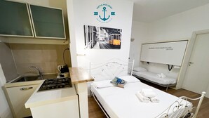 Una habitación de hotel compacta con kitchenette, una cama con almohada azul y un televisor de pared.
