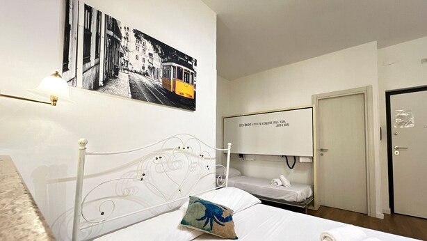 Habitación de hotel con cama, mesita de noche, televisor en la pared y una puerta.