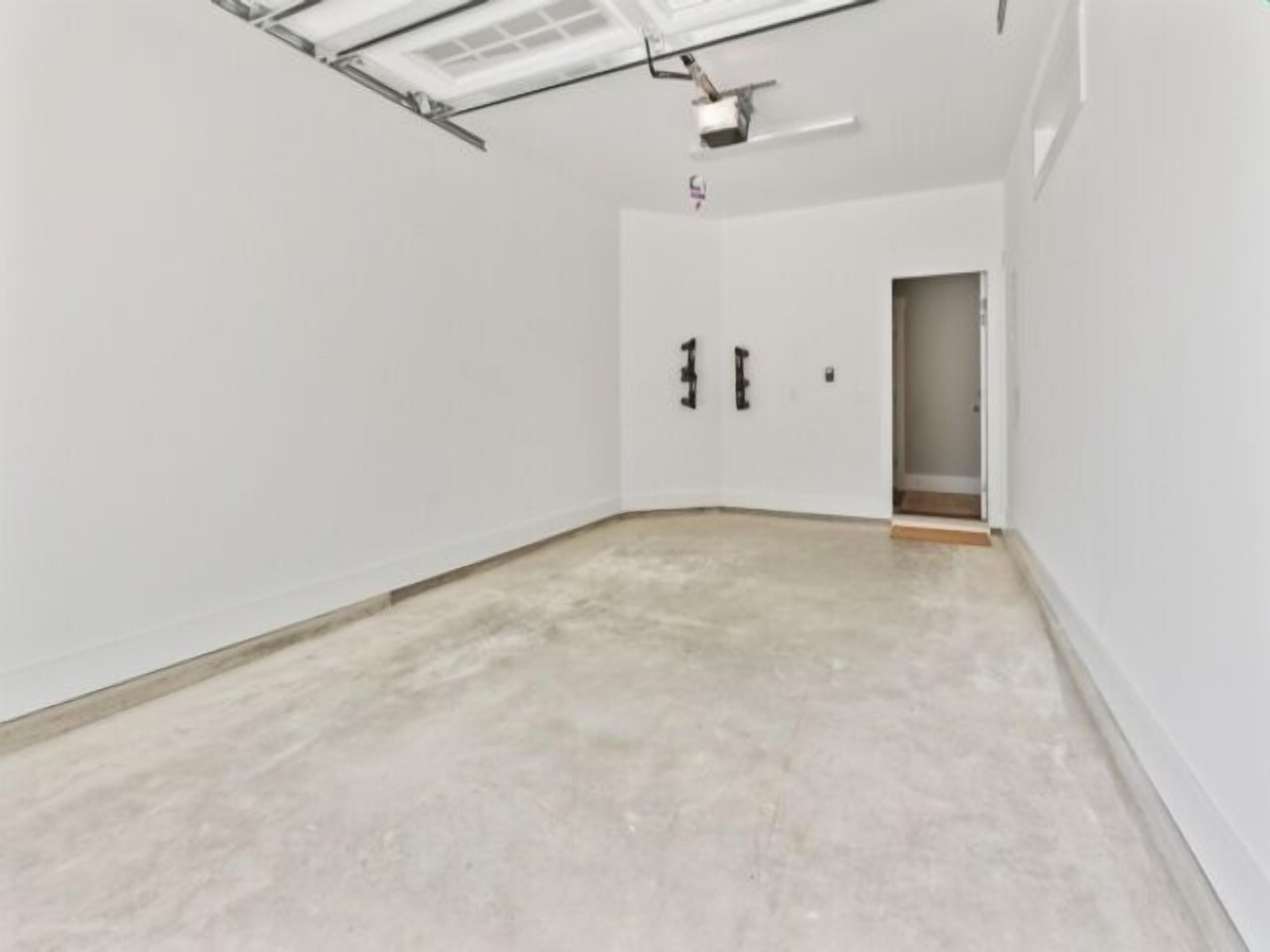Una habitación con paredes blancas, piso de concreto y una puerta con pomos negros.