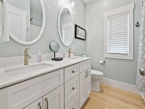Un bagno con un mobile lavabo bianco, due lavandini, un water e una finestra con persiane.