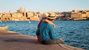 Una pareja sentada junto a la orilla, con un paisaje urbano al fondo.