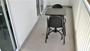 Un pasillo con una mesa, sillas, un vidrio y una barandilla blanca.