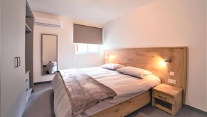 Une chambre à coucher avec un lit en bois, une table de chevet, un miroir et une fenêtre avec un store.