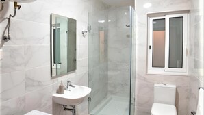 Une salle de bain moderne dotée d’une douche à parois de verre, d’un lavabo encastré, de toilettes et d’un lave-linge.