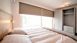 Una habitación de hotel moderna con una cama grande, un vestidor y vistas a la ciudad a través de amplios ventanales.