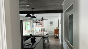 Moderni keittiö, jossa on keskellä sijaitseva saareke, riippuvalaisimet ja ruokailutila tuoleineen.