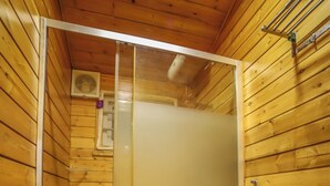 A wooden-paneled bathroom with a glass-enclosed shower, a toilet, and a sink.