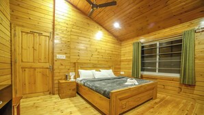 A wooden cabin room with a bed, a nightstand, a window with curtains, and a ceiling fan.