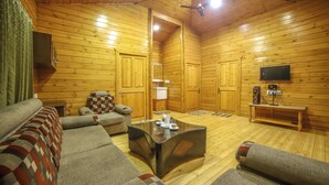 A cozy log cabin interior with a sofa, a glass coffee table, and a television on a wooden stand.