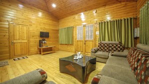 A wooden interior with a sofa, a glass coffee table, and a television.