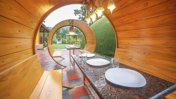 A wooden dining area with a table set for two, a bench, and a view through a semi-circular archway.