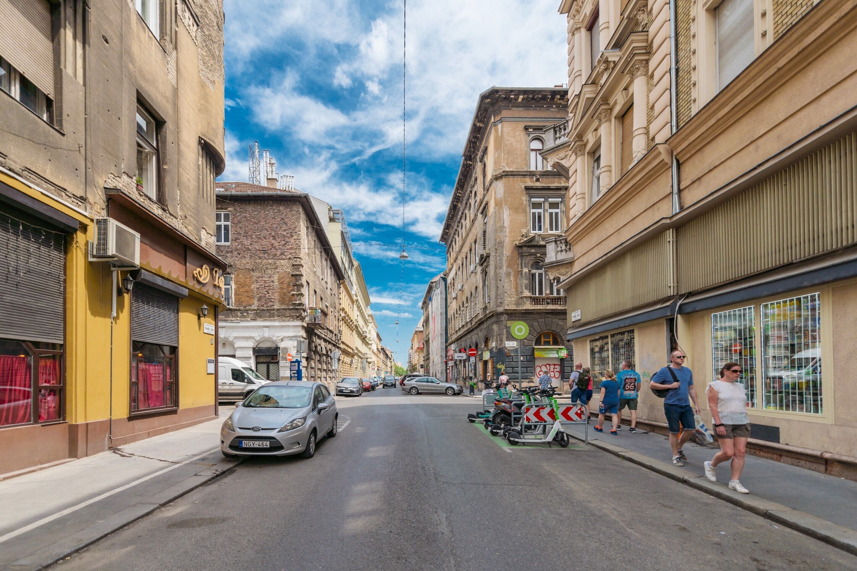 Eine Straße mit Gebäuden, parkenden Autos und Fußgängern.