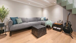 Ein modernes Wohnzimmer mit einem grauen Ecksofa, einem Marmor-Couchtisch, einer Gitarre und einer Treppe mit grünen Geländern.
