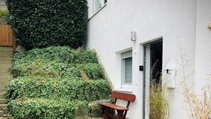 Un patio empedrado con un banco, plantas en macetas y un seto.