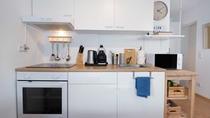 Cocina compacta con alacenas blancas, estufa, microondas y cafetera.