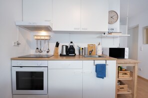 Cocina compacta con alacenas blancas, estufa, microondas y cafetera.