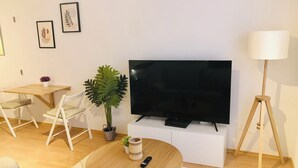 Una sala de estar con televisión, una mesa de centro redonda, una planta y una lámpara de pie blanca.