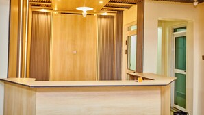 Un espace d’accueil moderne avec un comptoir de réception en bois, des stores verticaux et un luminaire au plafond.